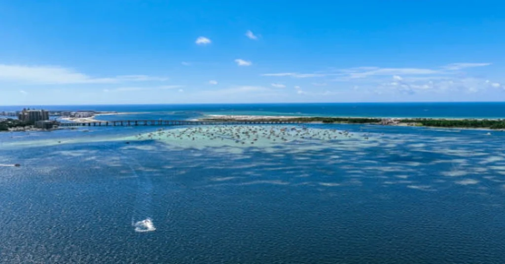 Aerial view of Miramar Beach, Florida, featuring clear blue waters, a scenic bridge, and boats scattered across the shoreline.