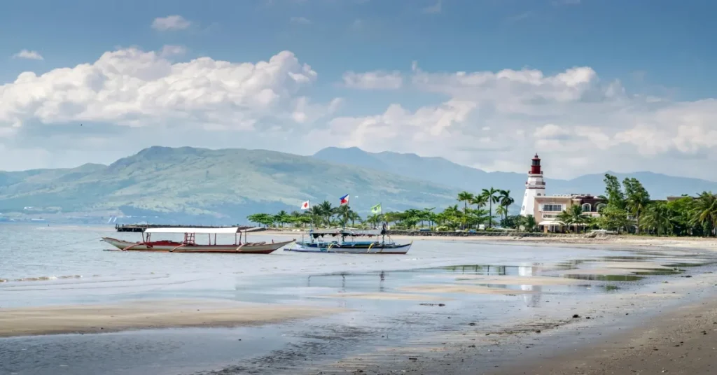 A scenic view of Subic Beach with crystal-clear waters, white sandy shores, and lush greenery under a vibrant blue sky.